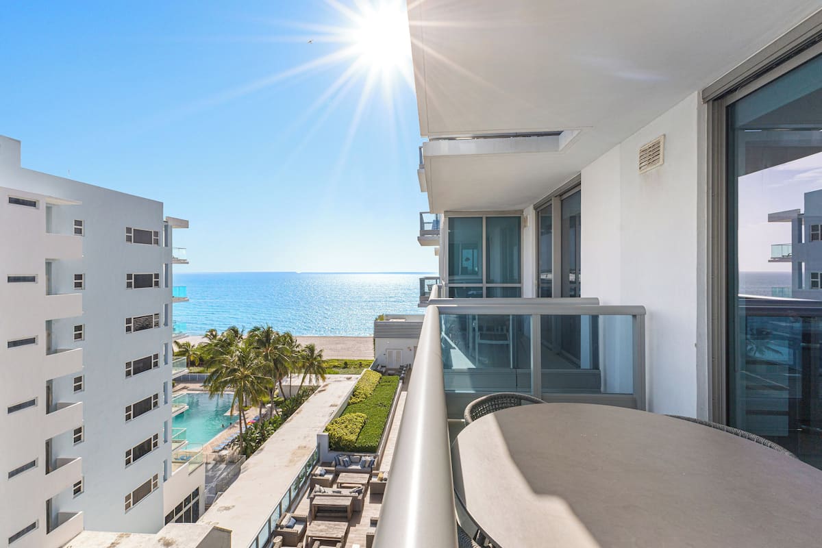 A modern hotel balcony with a view of the ocean and a pool area.
