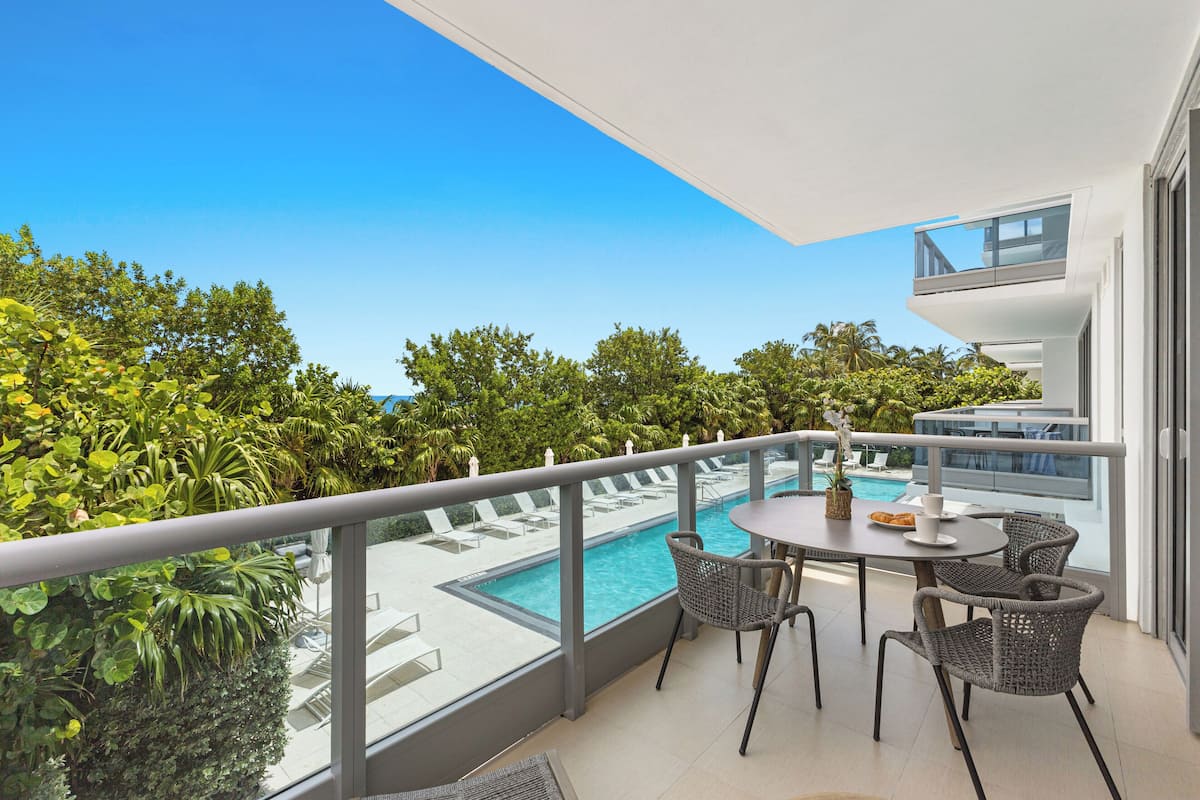 A balcony with a pool, wicker chairs, and a table with a drink.