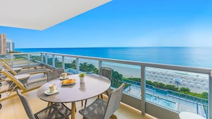 A balcony with a view of the ocean and beach, furnished with wicker chairs and a table with a plant and a plate of fruit. - Dharma Home Suites Miami at Monte Carlo (Miami Beach)