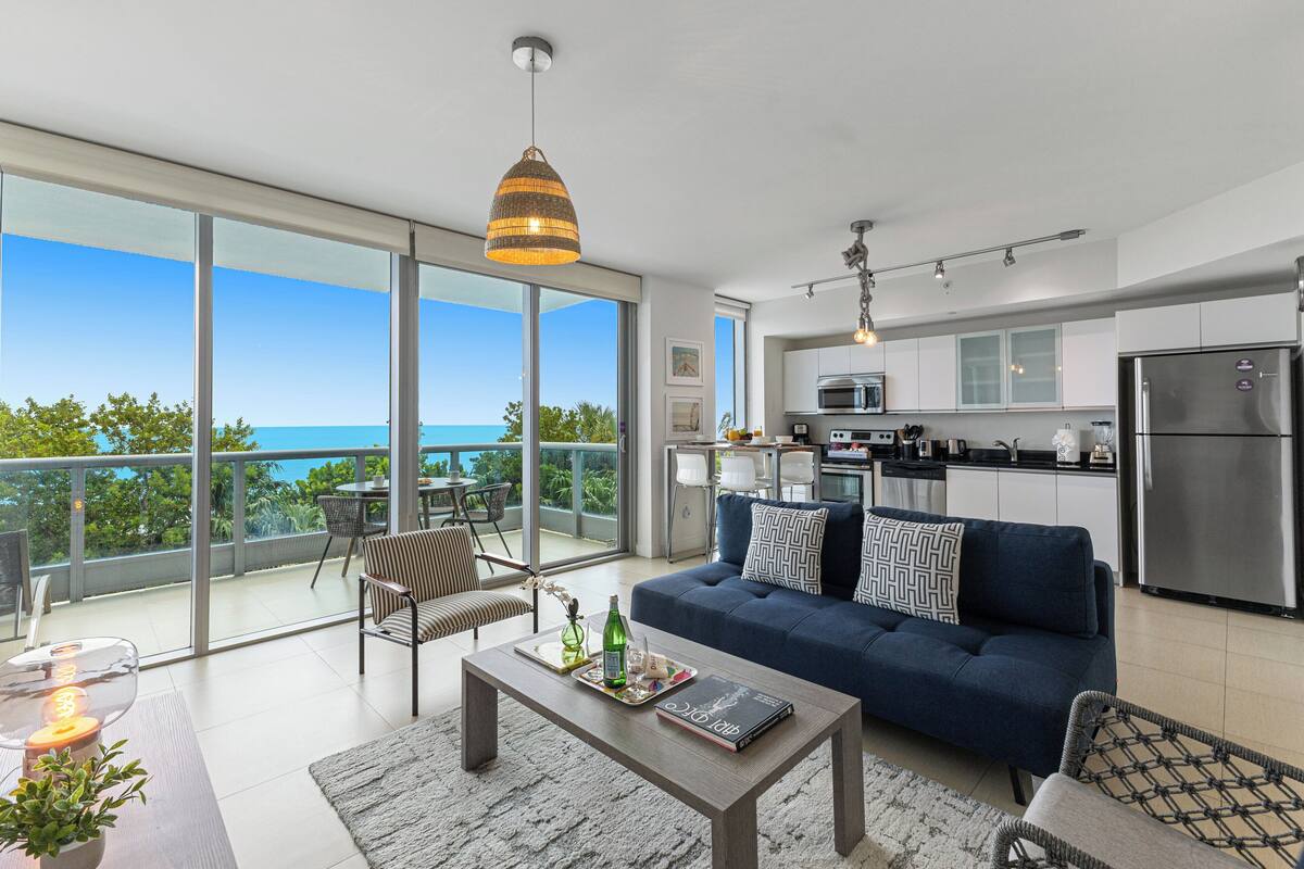 A modern apartment with a balcony, a kitchen, and a living area with a sofa and coffee table.