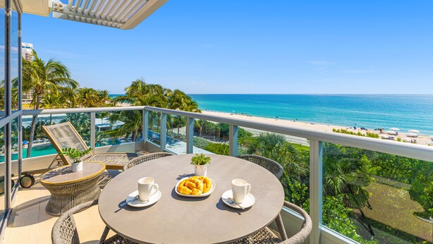 A balcony with a table set for two, overlooking a beach and ocean. - Dharma Home Suites Miami at Monte Carlo (Miami Beach)