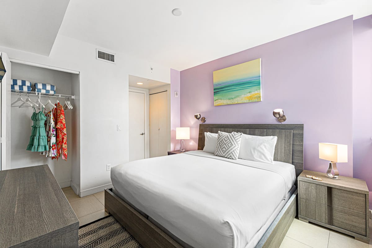 A bedroom with a bed, nightstands, a wardrobe, and a painting on the wall.