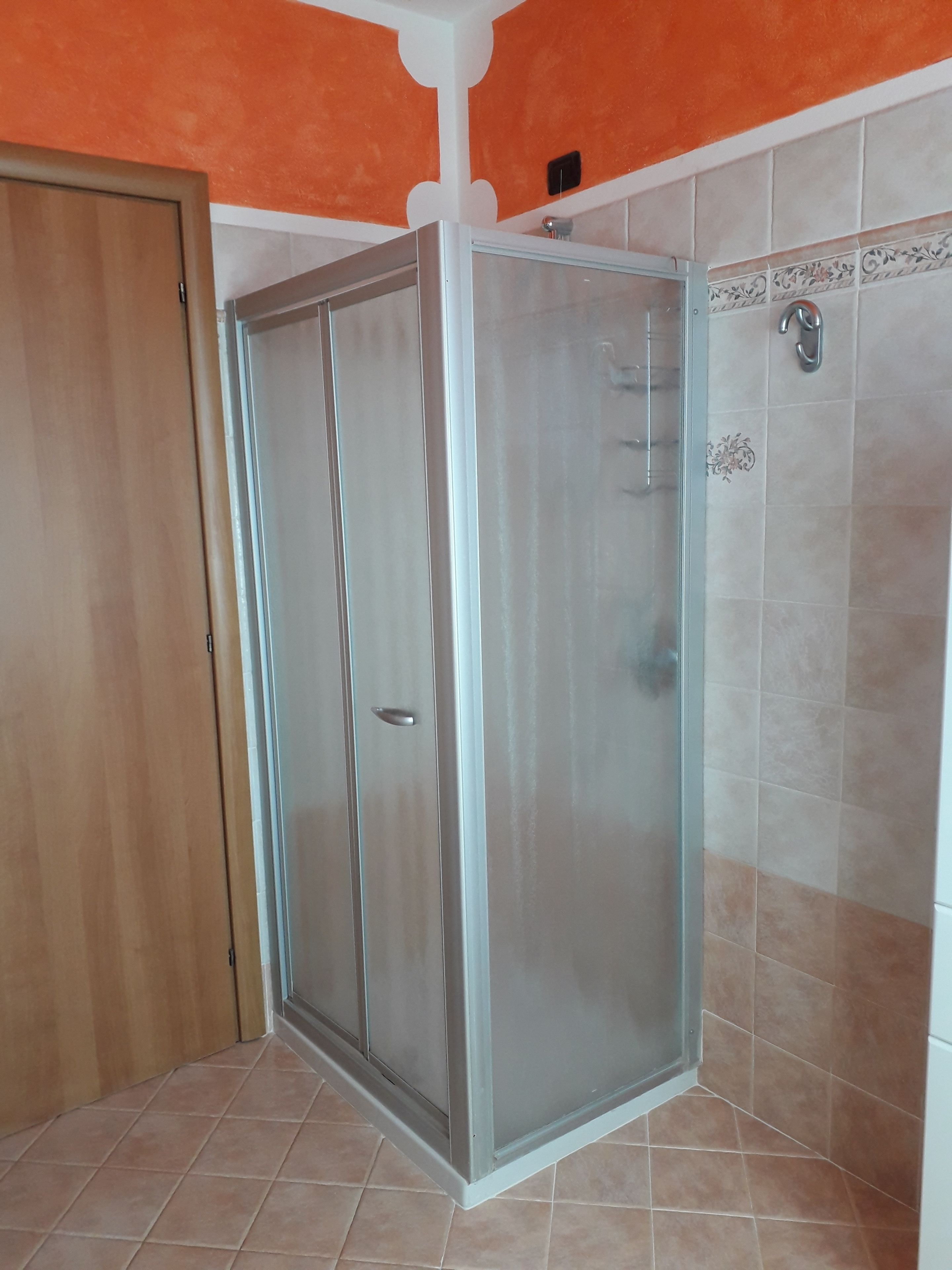 Un baño con cabina de ducha de vidrio, paredes enlosadas y una puerta de madera.