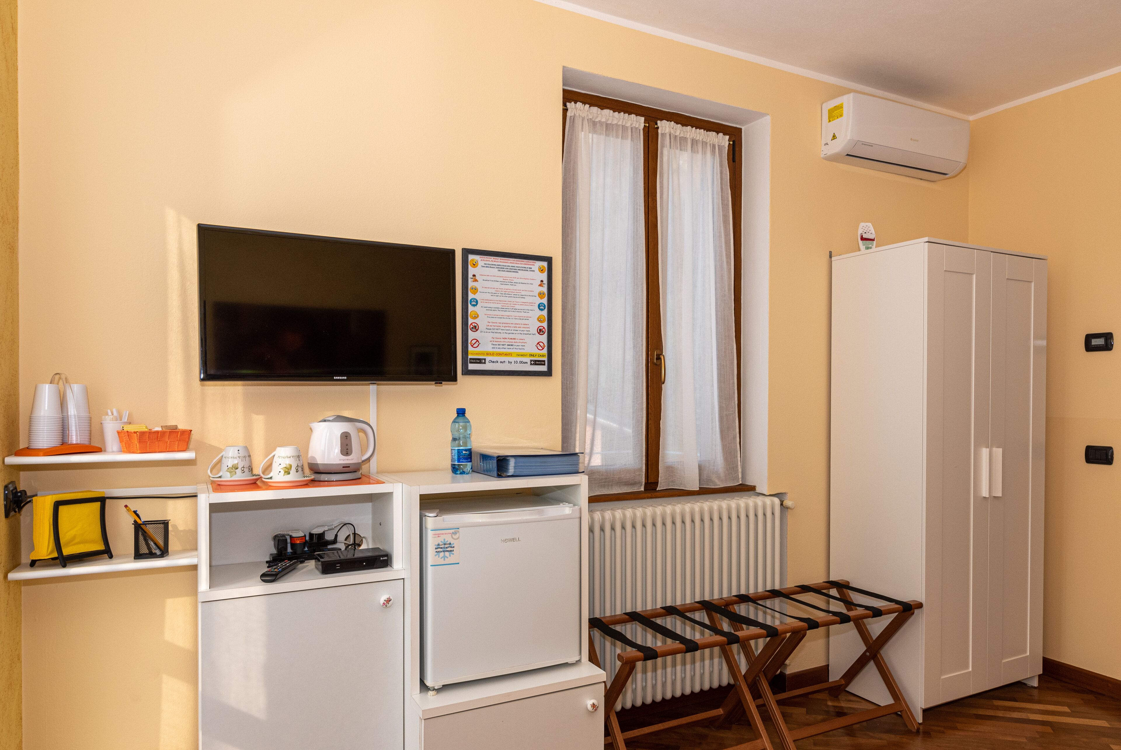 Una stanza compatta con TV, un piccolo frigorifero, un termosifone, uno stendibiancheria e un armadio.