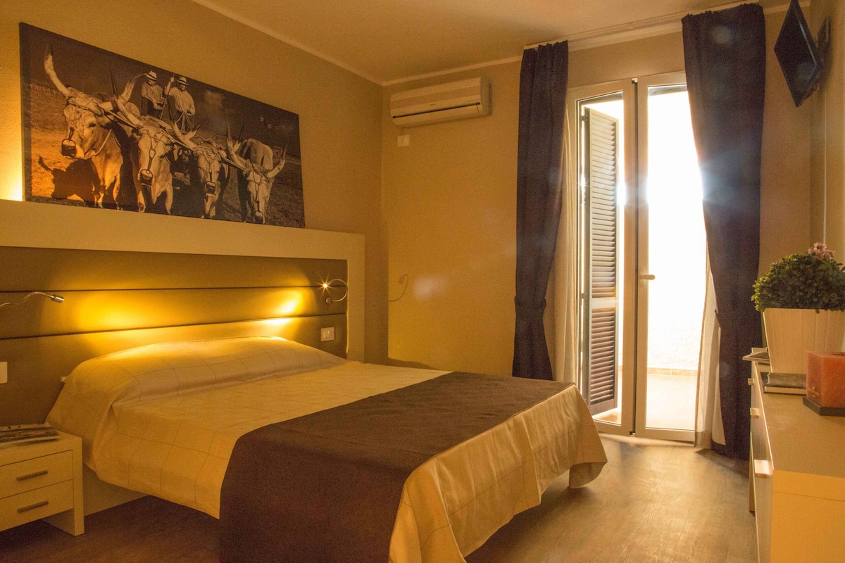 Ein Hotelzimmer mit einem Bett, einem Nachttisch, einer Klimaanlage, einer Schiebetür und einem Bild an der Wand.