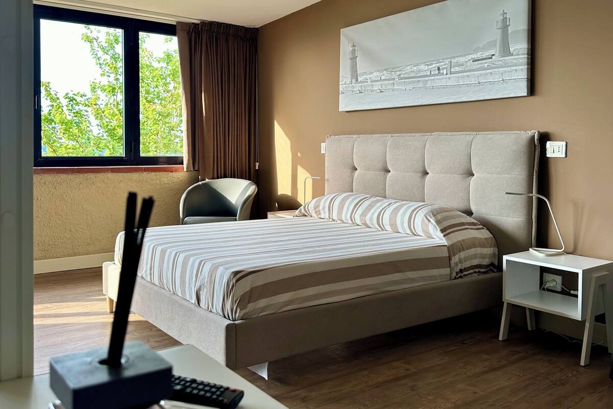 Ein modernes Schlafzimmer mit einem großen Bett, einem Nachttisch, einem Schreibtisch und einem Fenster mit Vorhängen.
