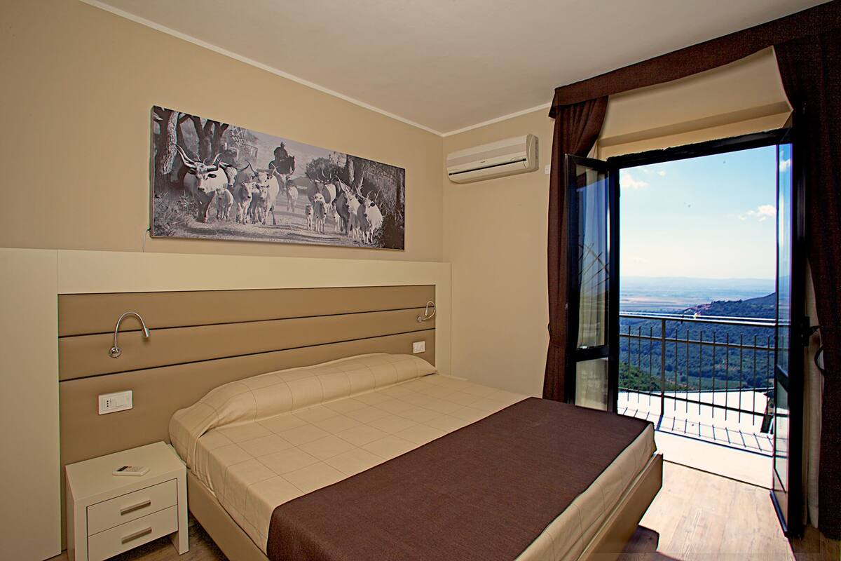 Ein Schlafzimmer mit einem Bett, einem Nachttisch, einem Gemälde, einer Klimaanlage und einem Balkon mit Blick.