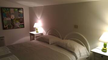 A bedroom with a bed, two bedside tables, a nightstand, a wall-mounted artwork, and a lamp on each bedside table.