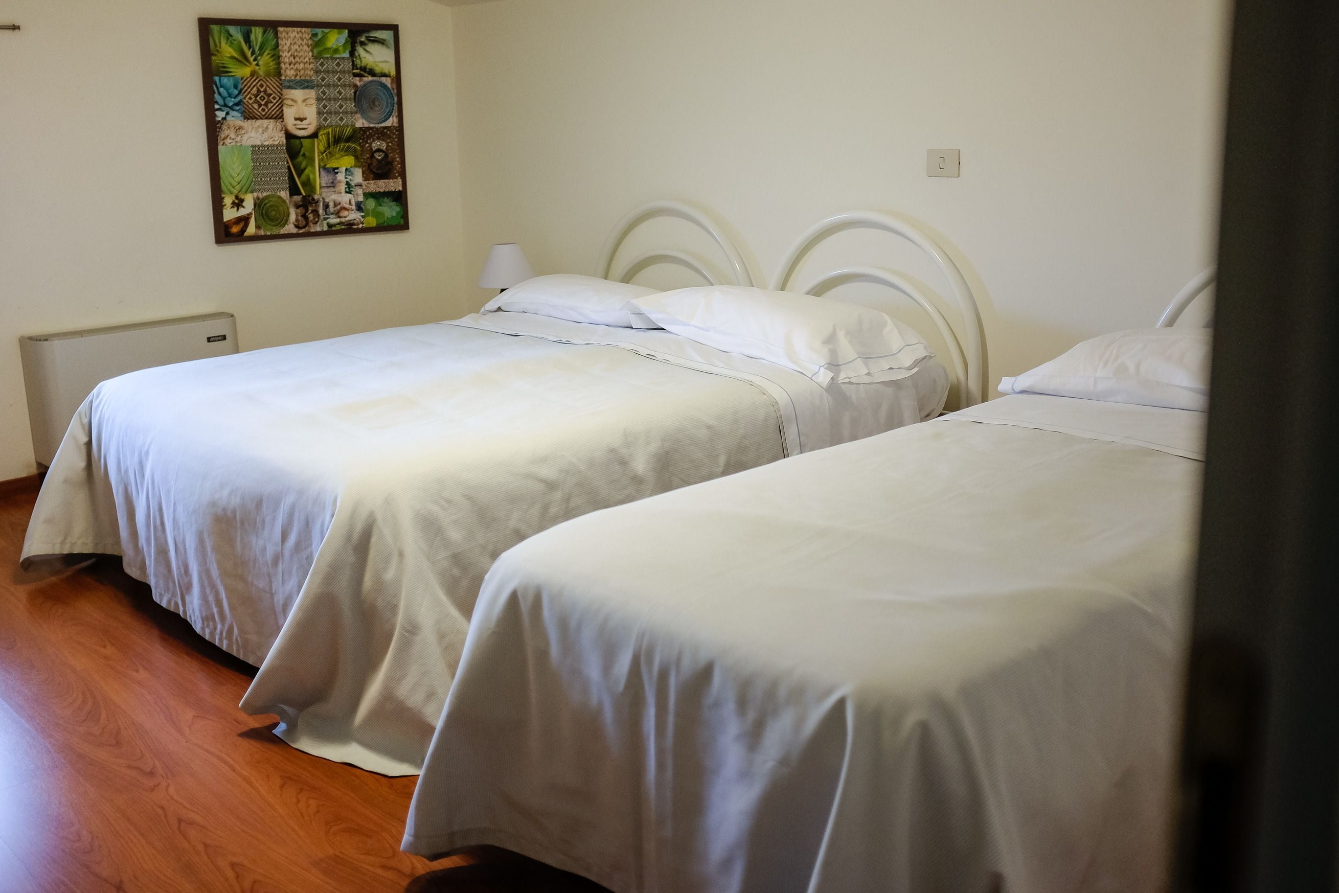 Duas camas de solteiro com roupa de cama branca em quarto com soalho de madeira e uma obra de arte na parede.