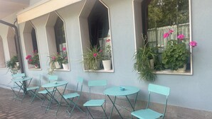 A row of teal chairs and tables outside a building with arched windows and potted plants. - Hotel L'Approdo (Cesenatico)