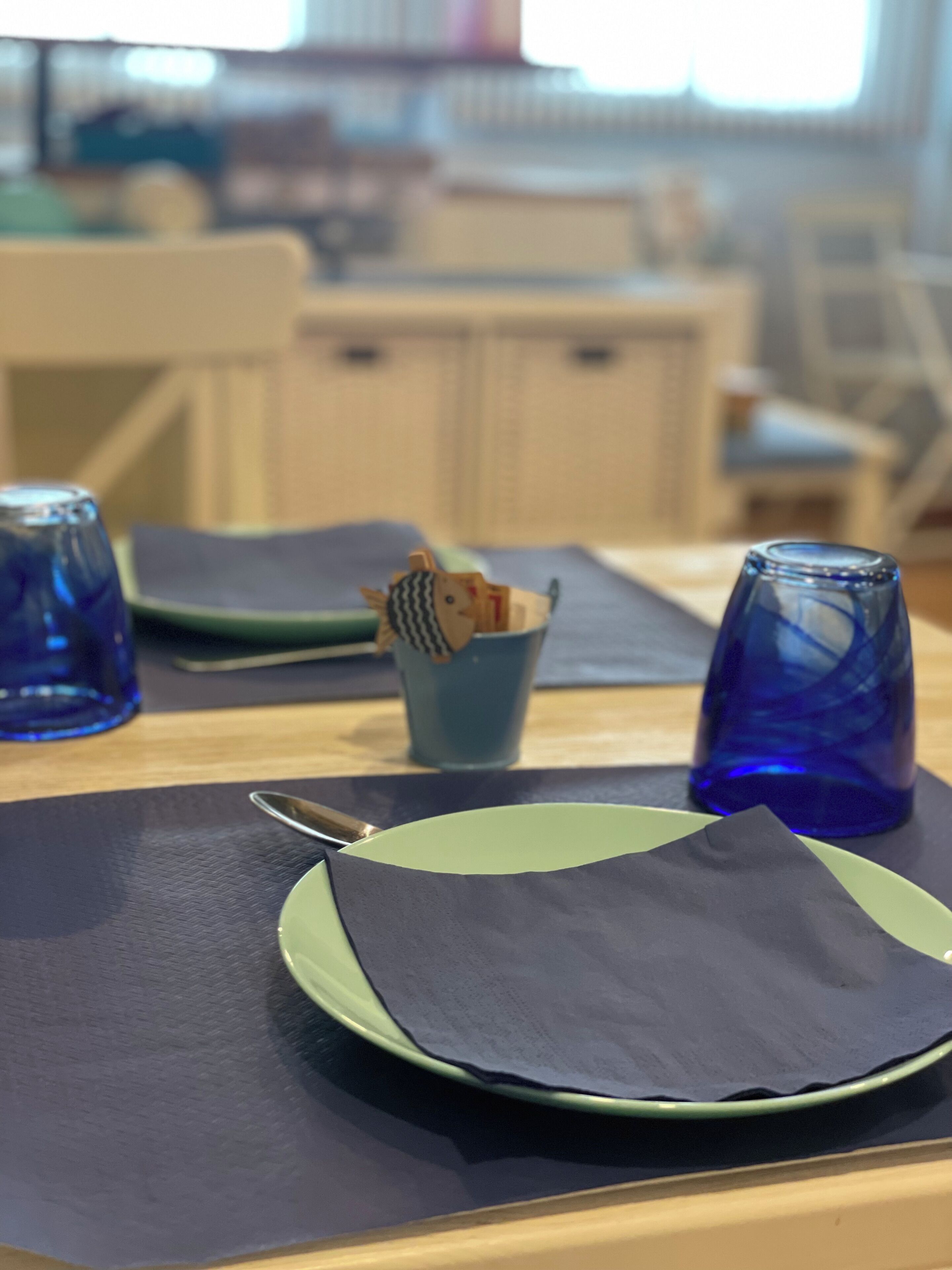 A dining table with a green plate, a dark napkin, and a blue glass.