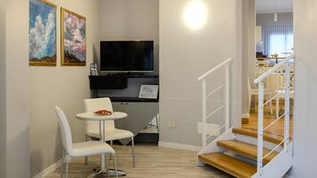 A modern living space with a flat-screen TV, a small dining table with chairs, and a staircase.