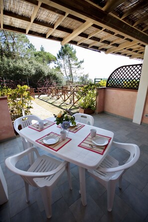 Un porxo exterior cobert amb taula per a quatre, envoltat de cadires de plàstic blanc.
