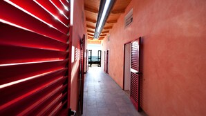 A hallway with red slatted walls and a tiled floor, leading to a door at the end. - Le Dune (Follonica)