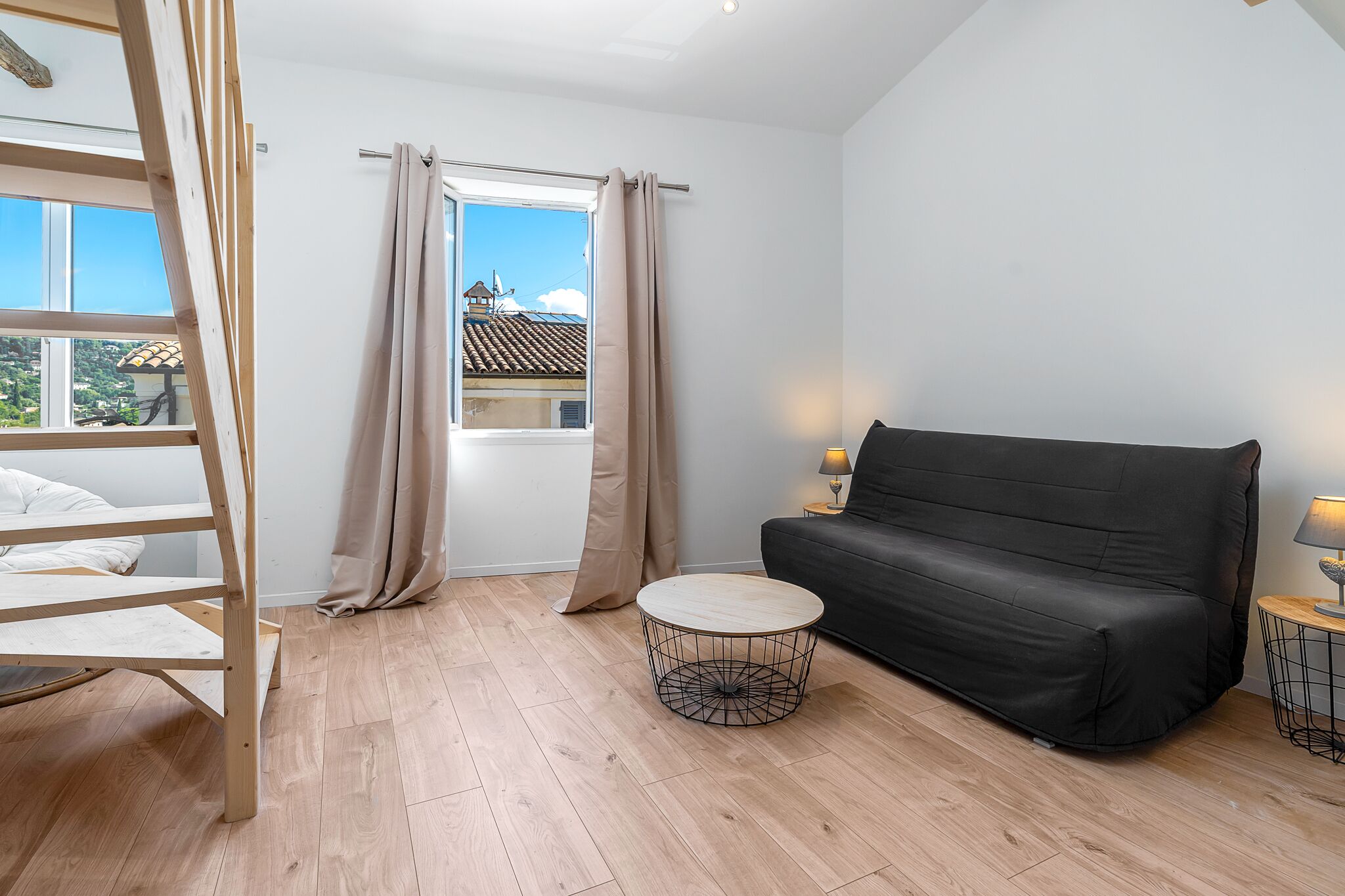 A room with a loft bed, a black sofa, a round coffee table, and a window with curtains.
