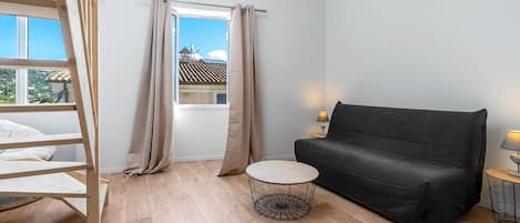 A room with a loft bed, a black sofa, a round coffee table, and a window with curtains.