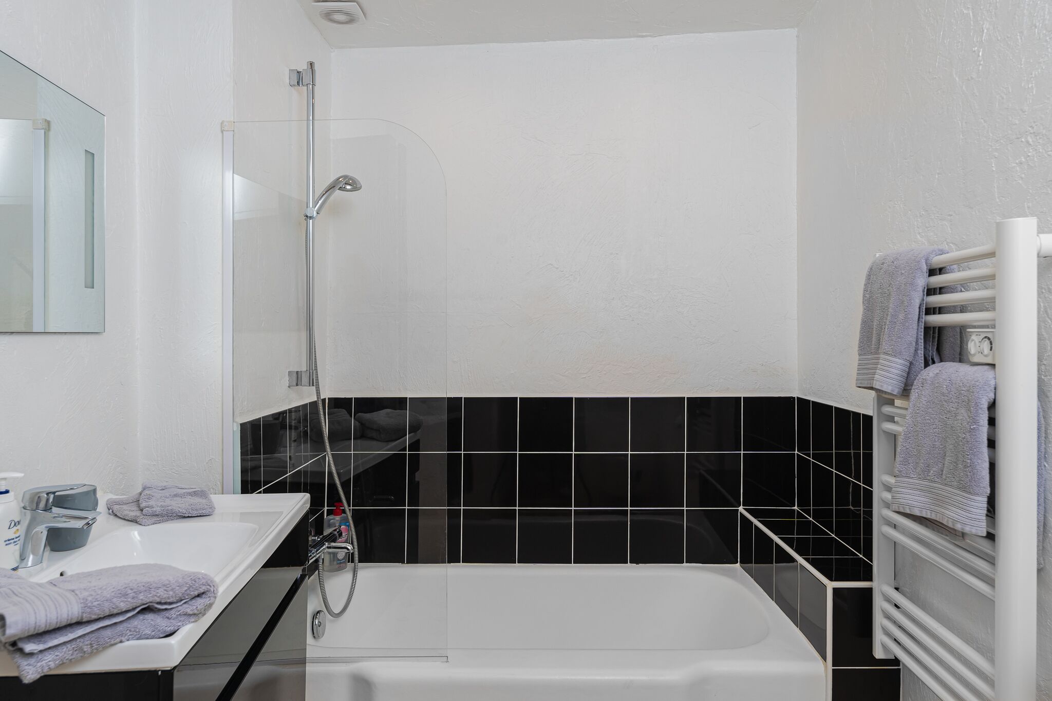 A modern bathroom with a glass shower enclosure, a white bathtub, and a black tiled backsplash.