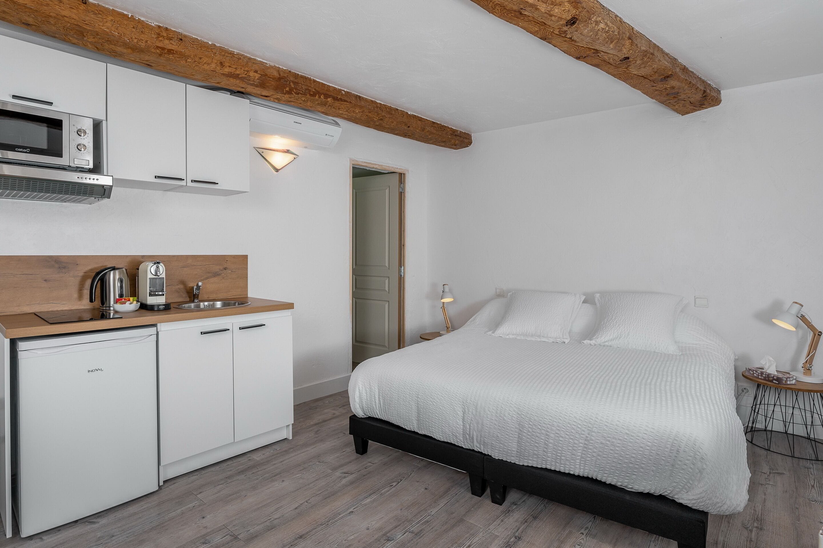 A compact bedroom with a bed, bedside table, and a small kitchenette.