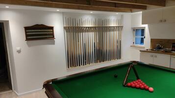 A pool table with a green felt surface, a clock on the wall, and a window with blinds.
