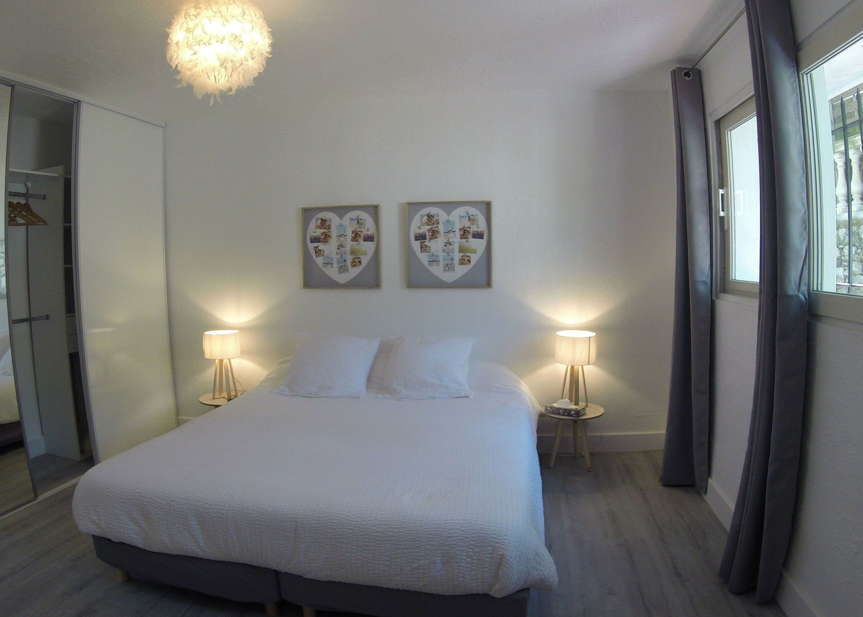 Un dormitorio con cama, dos lámparas de noche, una araña y decoración de pared con forma de corazón.