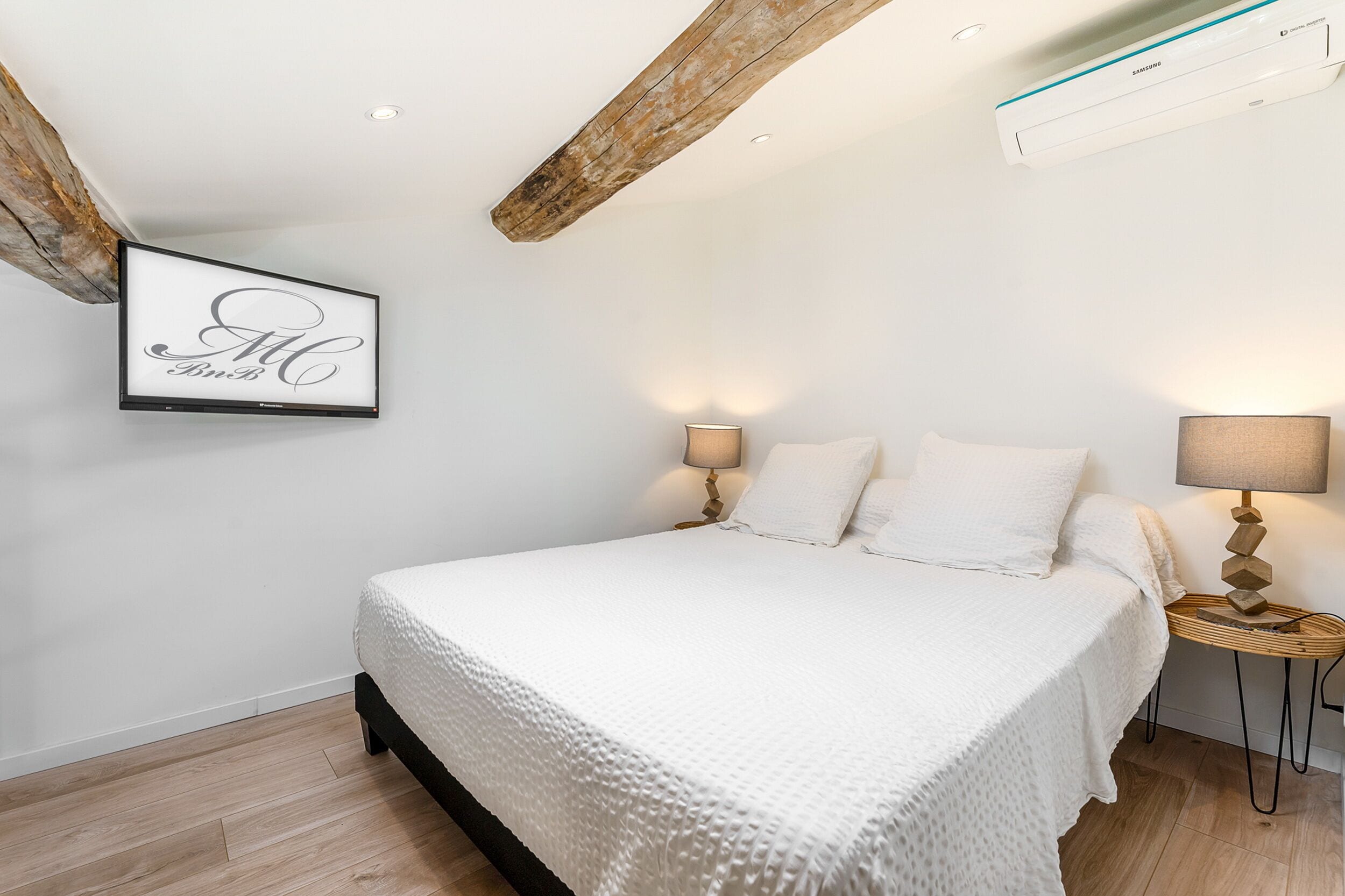 Een slaapkamer met een groot bed, twee bedlampen, een lijst aan de muur en zichtbare houten balken.