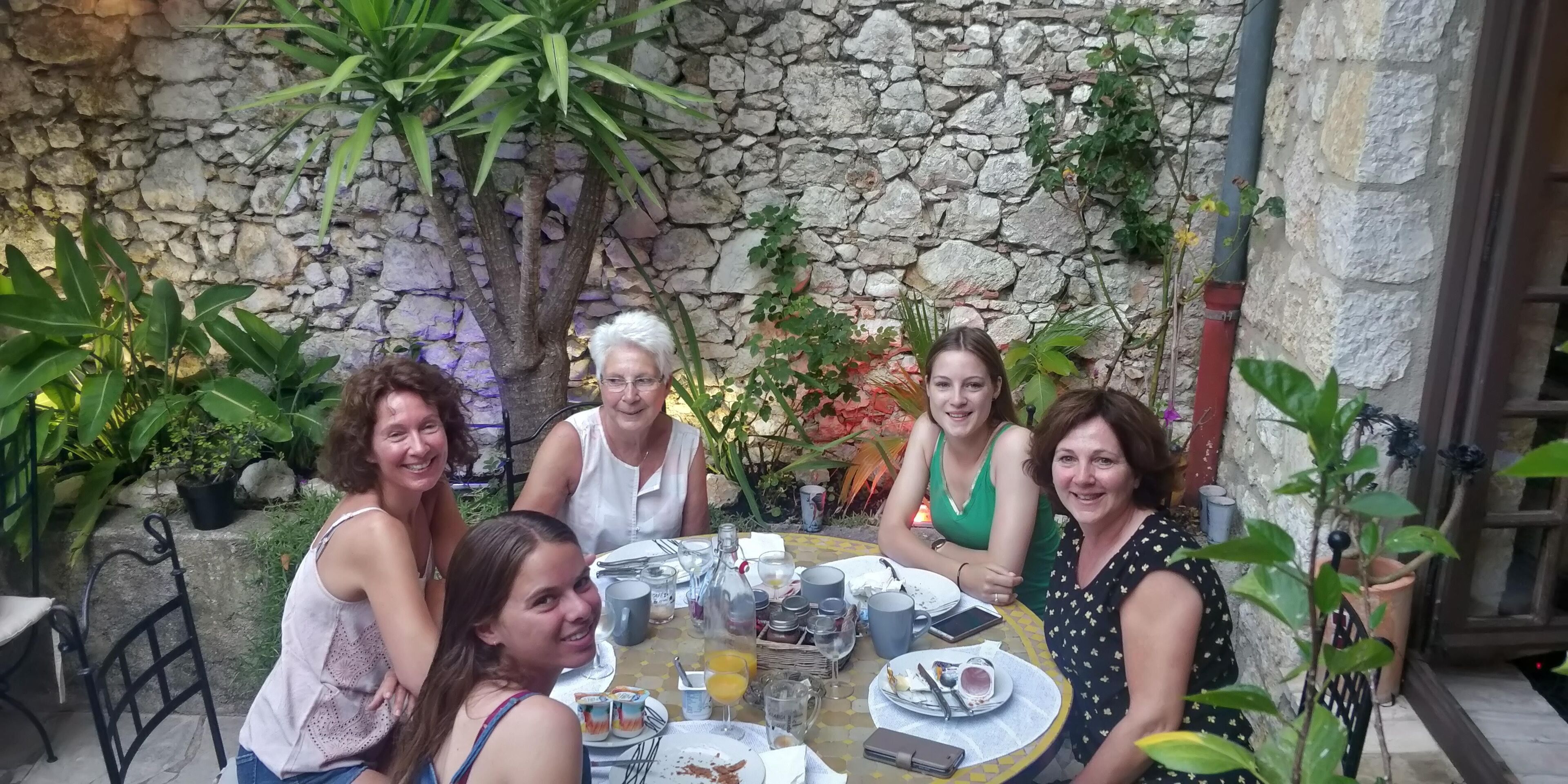 A group of people seated around a table in an outdoor setting with stone walls and potted plants.