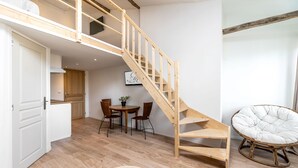 Ein Loft-Zimmer mit einer Holztreppe, einem Essbereich mit rundem Tisch und Stühlen sowie einem Rattanstuhl.