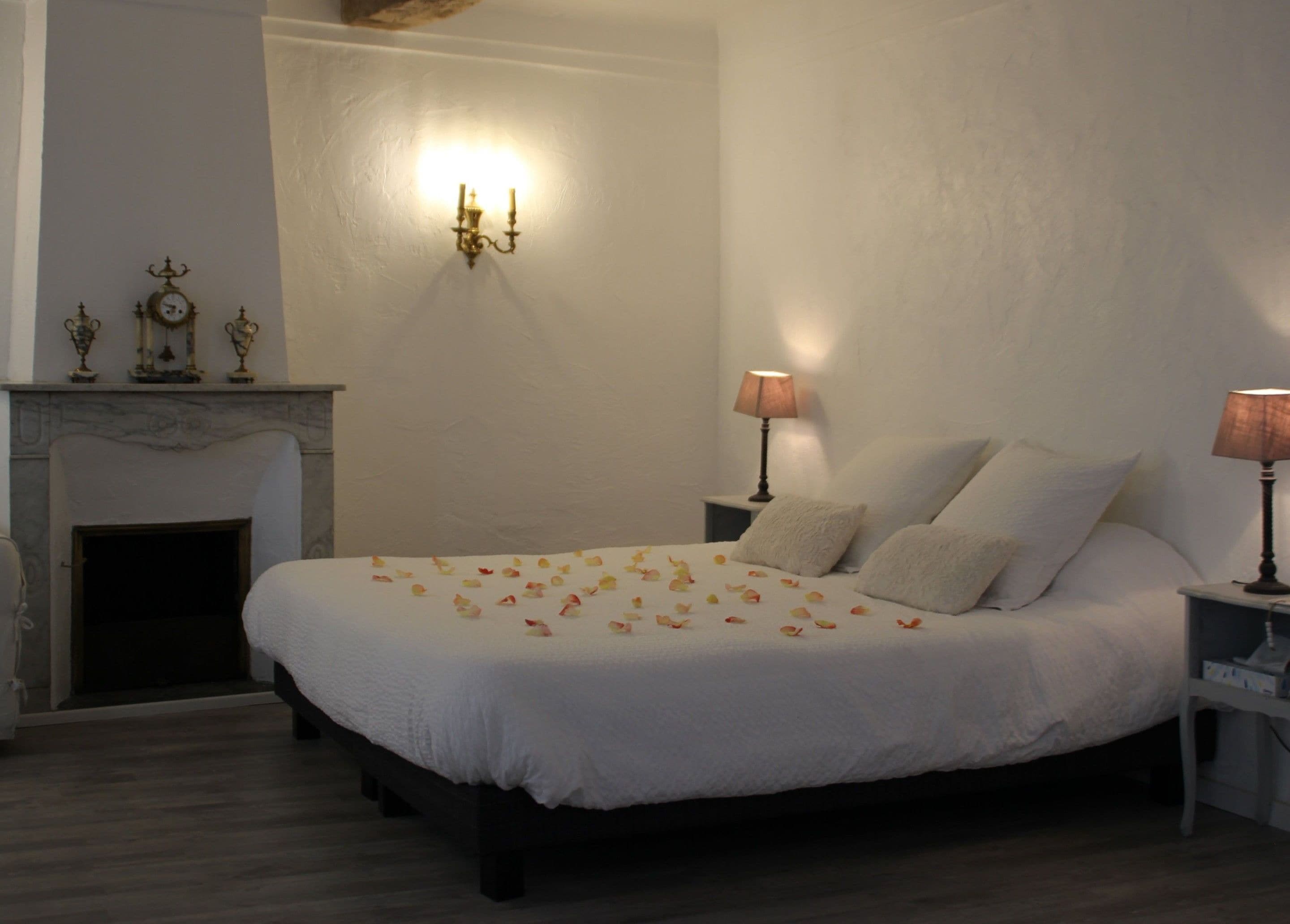 A bedroom with a large bed, a fireplace, and two bedside lamps.