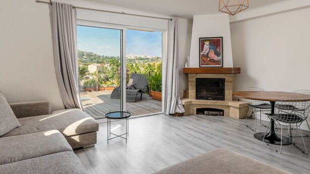 Ein modernes Wohnzimmer mit einer Couch, einem Esstisch mit Stühlen, einem Kamin und einer großen Glasschiebetür, die auf eine Terrasse im Freien führt.