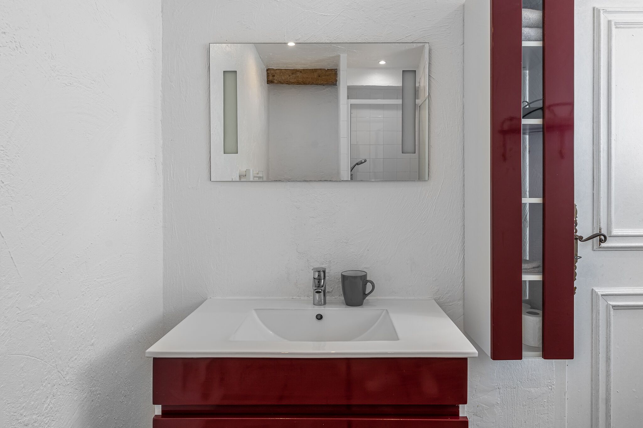 Un baño con un lavamanos blanco, un espejo y un mueble rojo.