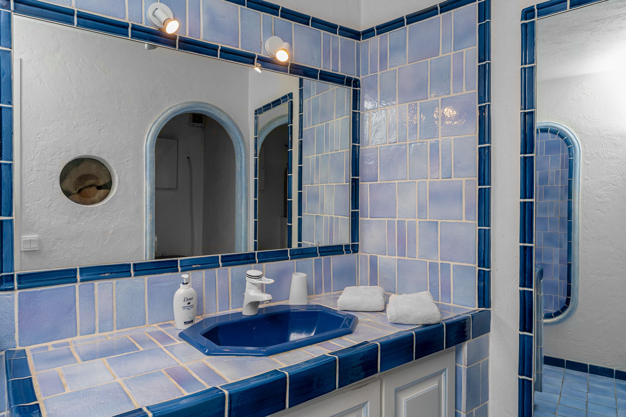 Un baño con un lavamanos de azulejos azules, un espejo grande y un perchero para toallas.