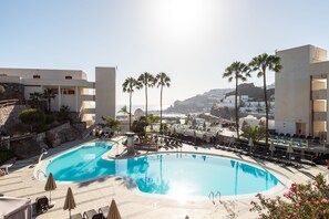 A resort pool area with a large pool, sun loungers, umbrellas, and palm trees. - Holiday Club Puerto Calma (Mogan)