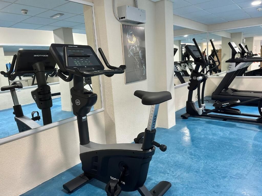 Une salle de sport équipée de vélos d’appartement et de tapis de course, avec des murs recouverts de miroirs et un sol bleu.