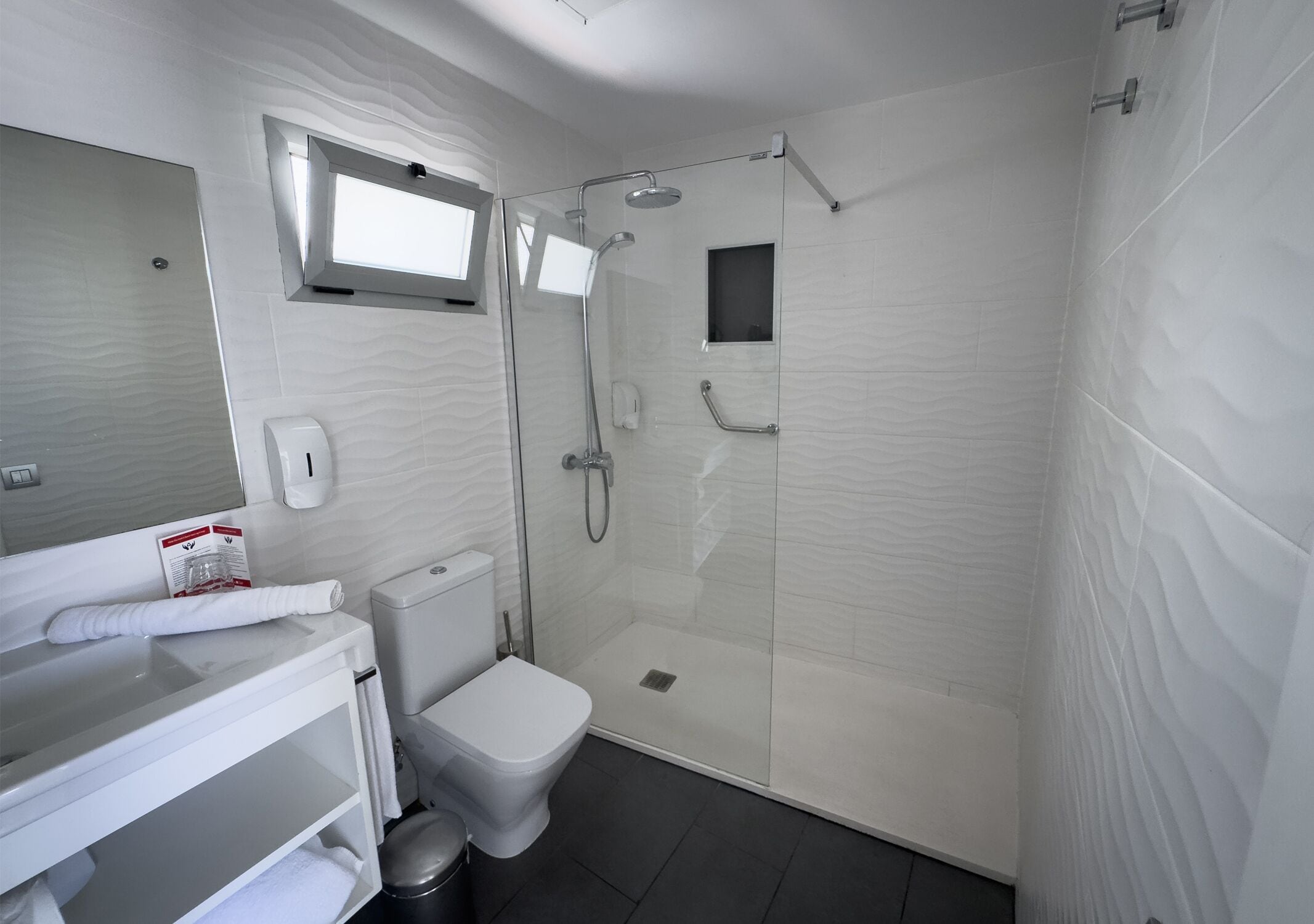 A modern bathroom with a glass-enclosed shower, a toilet, a sink with a towel, and a mirror.