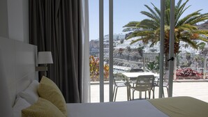 A hotel room with a large bed, a view of a coastal area, and a balcony with chairs.