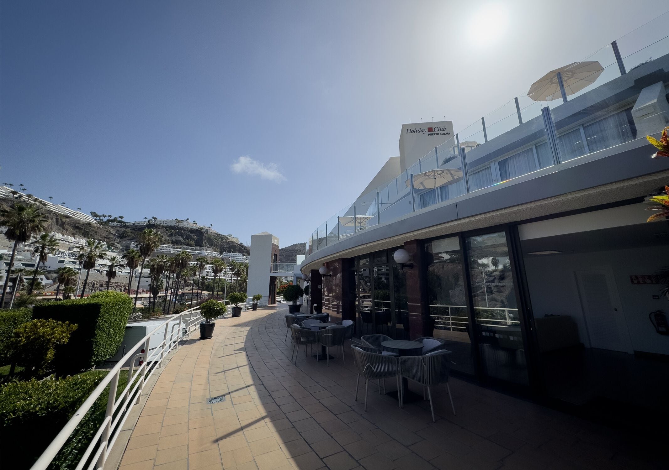 A hotel with outdoor seating, a clear view of the surrounding area, and a sign indicating it is a Holiday Club.