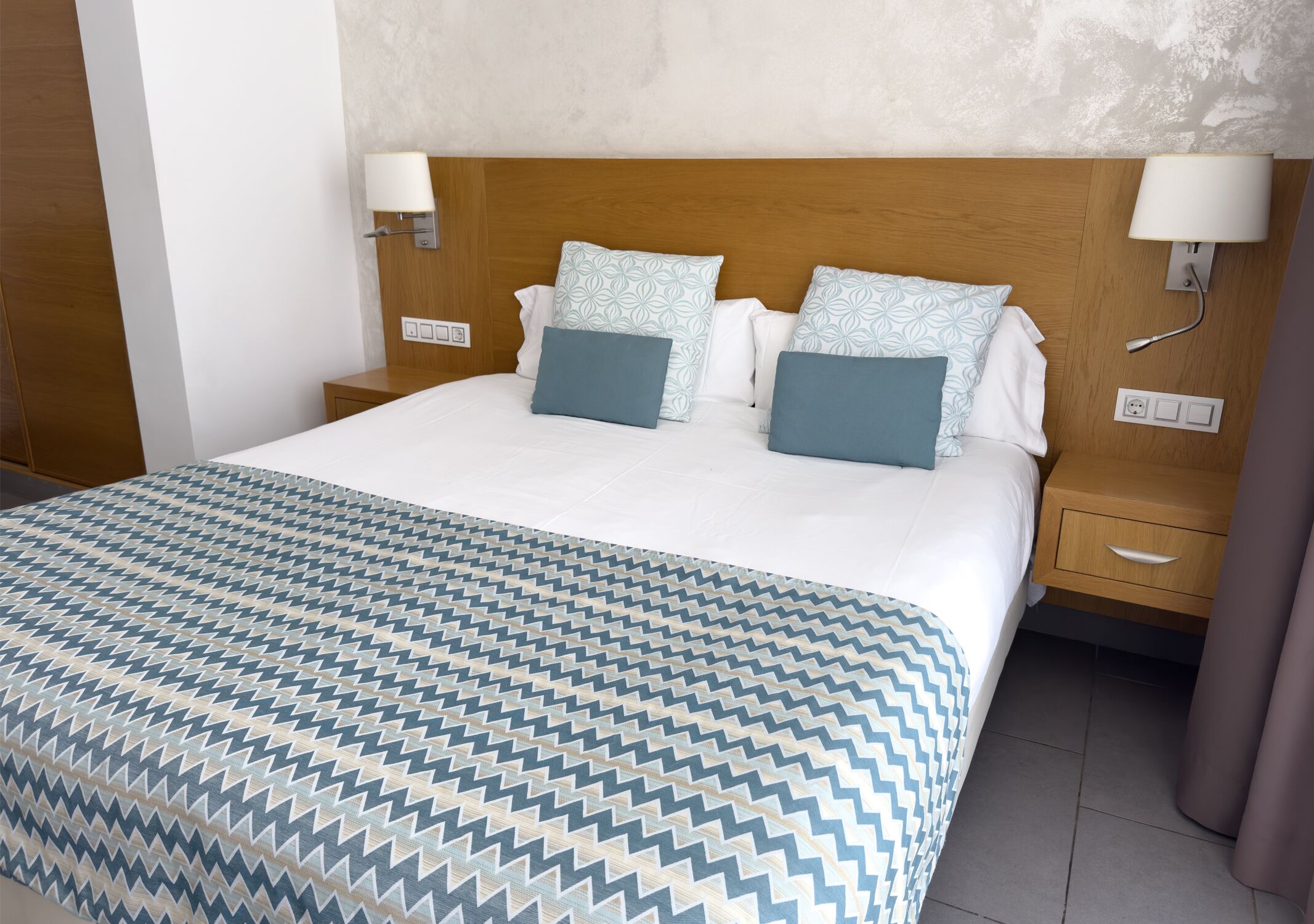A hotel room with a large bed, two bedside tables, and a wooden headboard.