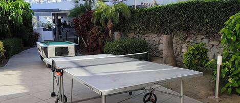 An outdoor table tennis table with wheels, surrounded by greenery and a building with a sign reading "Holiday Club Puerto Calima".