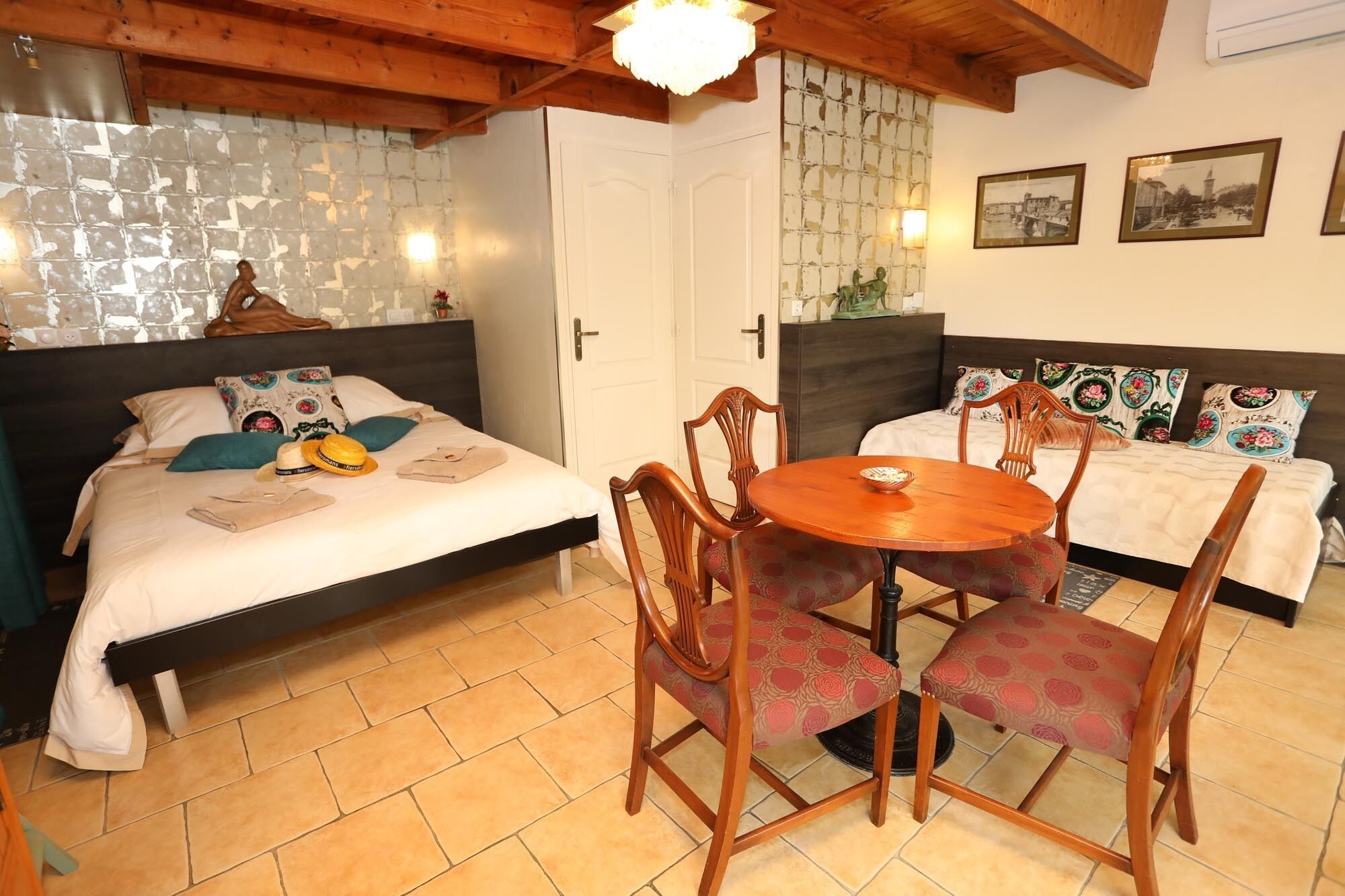 A cozy room with two beds, a wooden dining table, and a tiled floor.