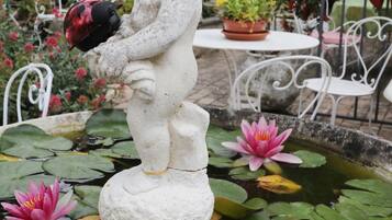 Una estatua de jardín de un niño sosteniendo un objeto rojo, rodeada de lirios acuáticos y plantas en macetas.
