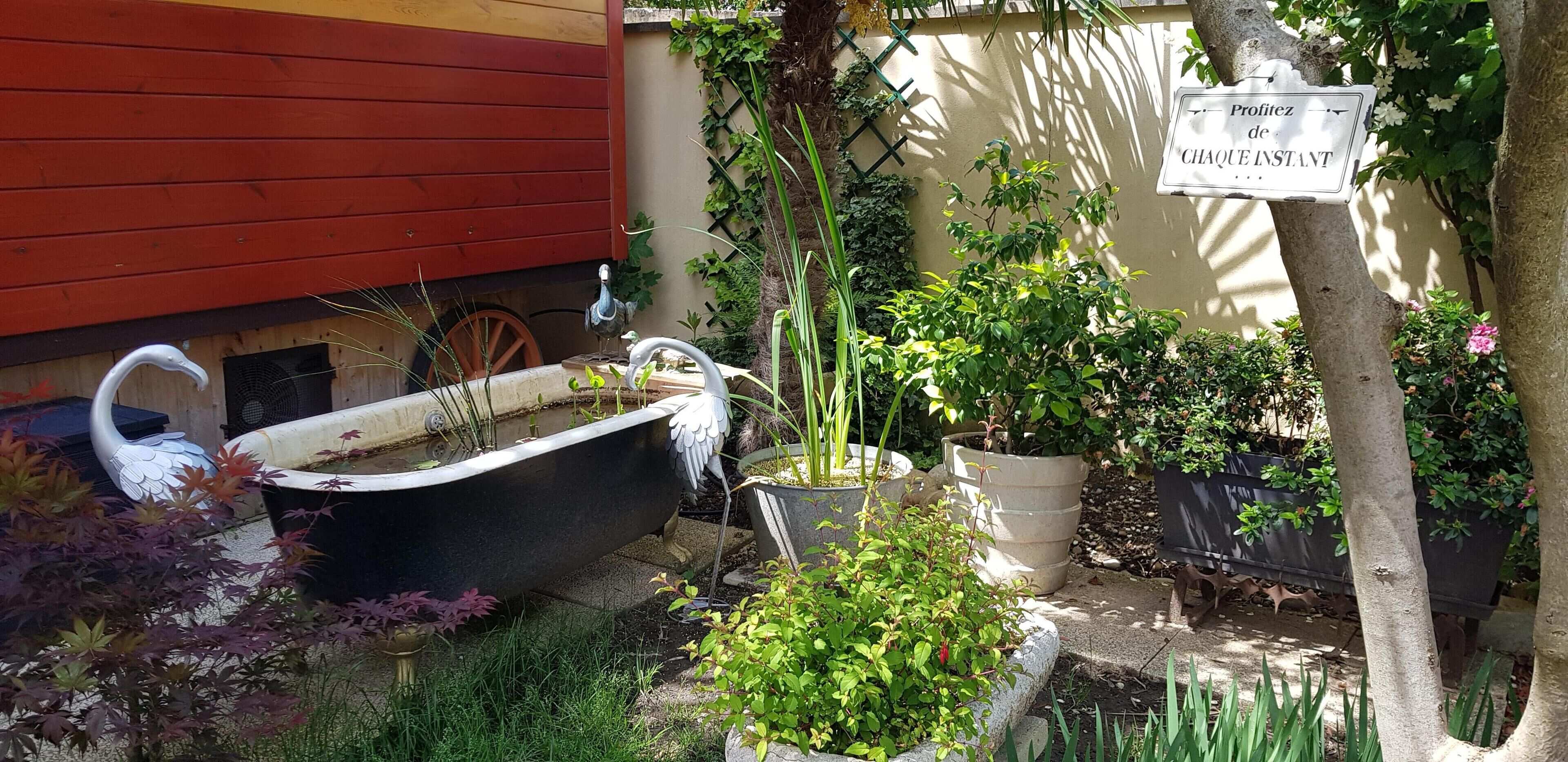 Un jardín con una bañera decorativa, plantas en macetas y un letrero en francés.