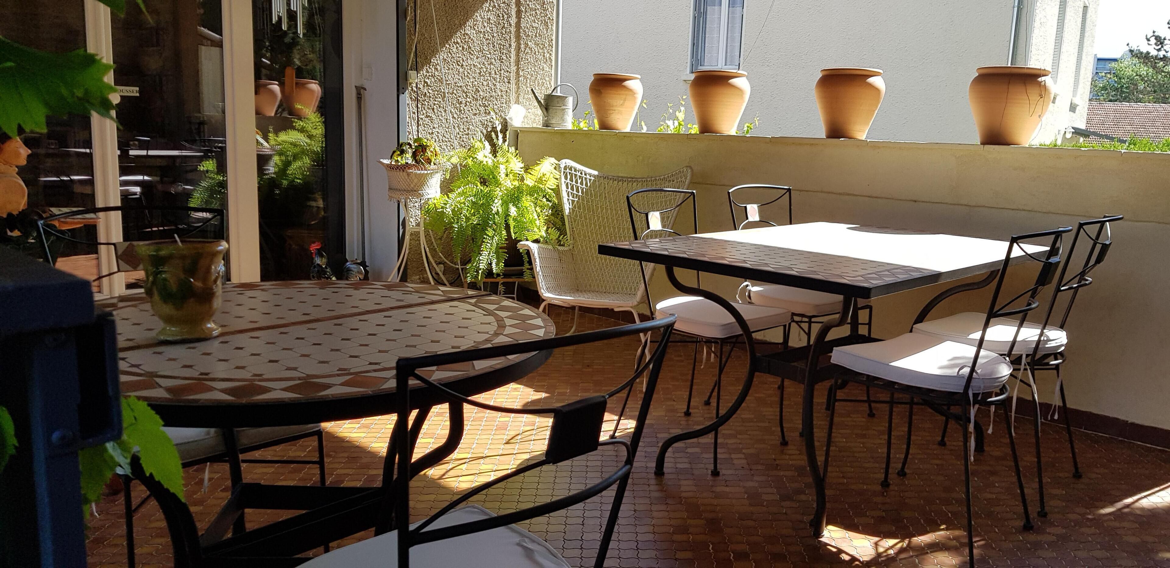 A patio area with a round table and chairs, potted plants, and terracotta pots on a balcony.