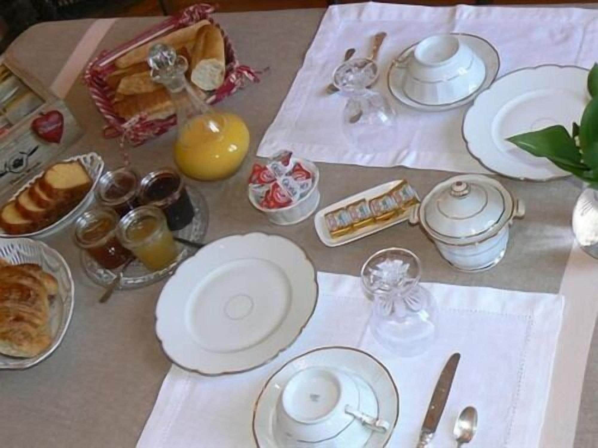 A breakfast table set with plates, cups, a knife, a fork, a teapot, a jug, and a basket of bread.