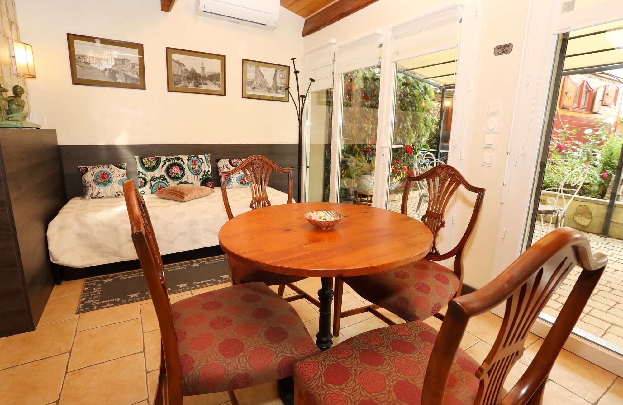 A cozy room with a bed, a dining table with chairs, and a balcony with plants.