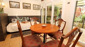 A cozy room with a bed, a dining table with chairs, and a balcony with plants.