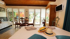 Une chambre avec un lit, un bureau et une chaise. Il y a une fenêtre avec des stores, un téléviseur fixé au mur et une porte donnant sur un balcon.