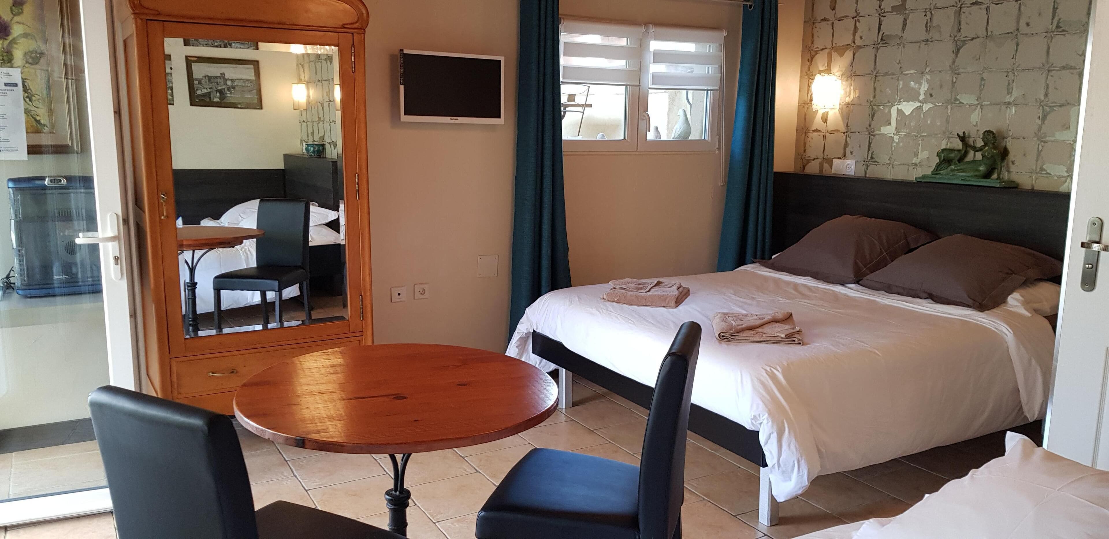 Habitación de hotel con cama, una mesa redonda de madera, dos sillas, televisor y ventana con cortinas.