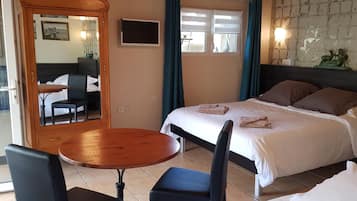Habitación de hotel con cama, una mesa redonda de madera, dos sillas, televisor y ventana con cortinas.
