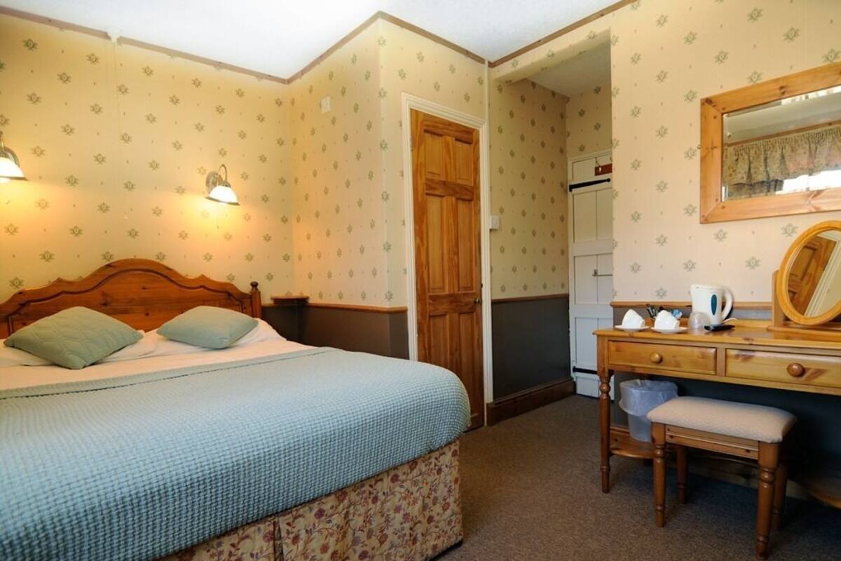 A bedroom with a bed, a wooden dresser, a mirror, and a door leading to another room.