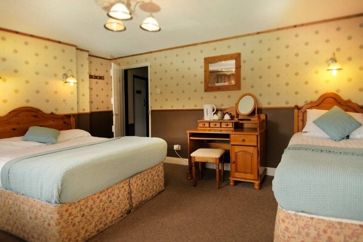 A room with two beds, a wooden desk, a chair, and a mirror.